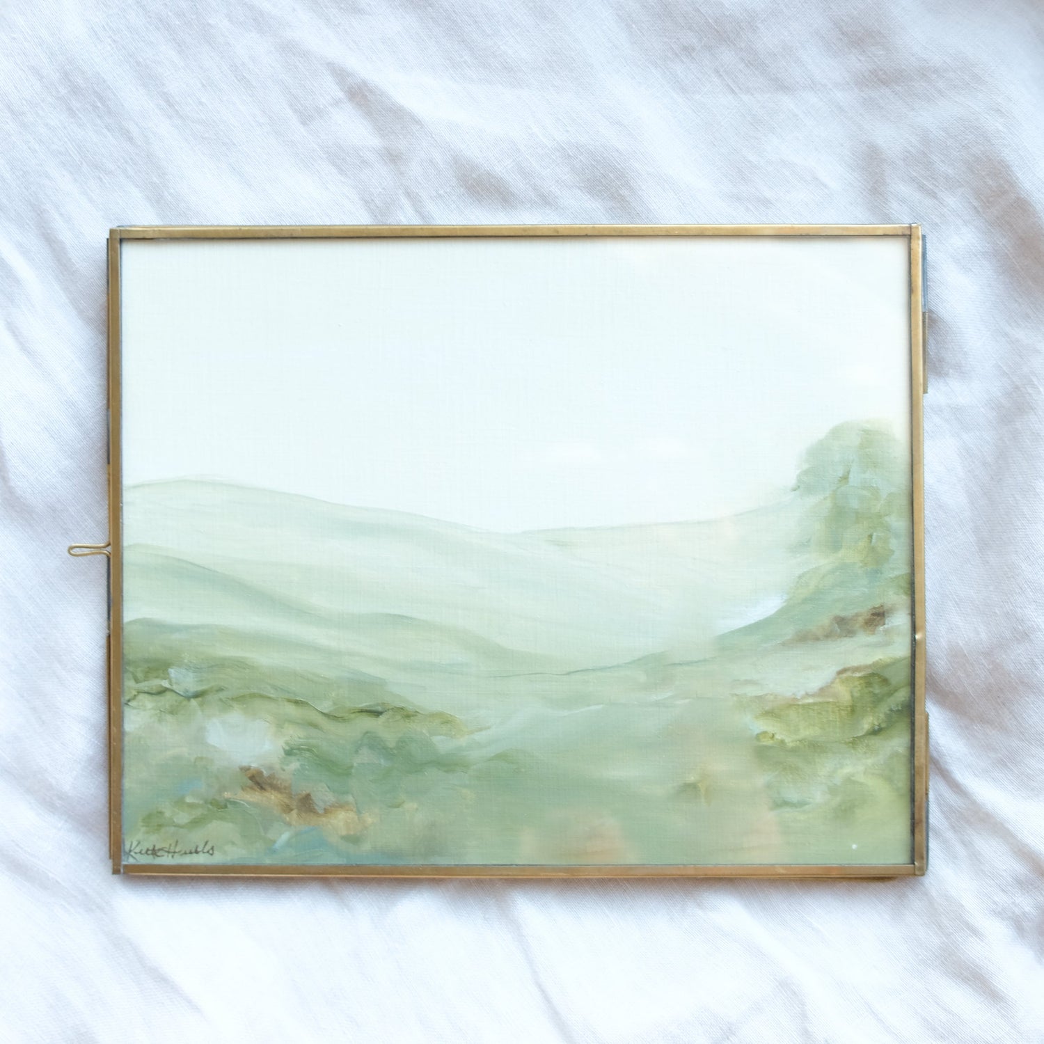 A framed landscape photo of an impressionist green hill and one tree in the distance.