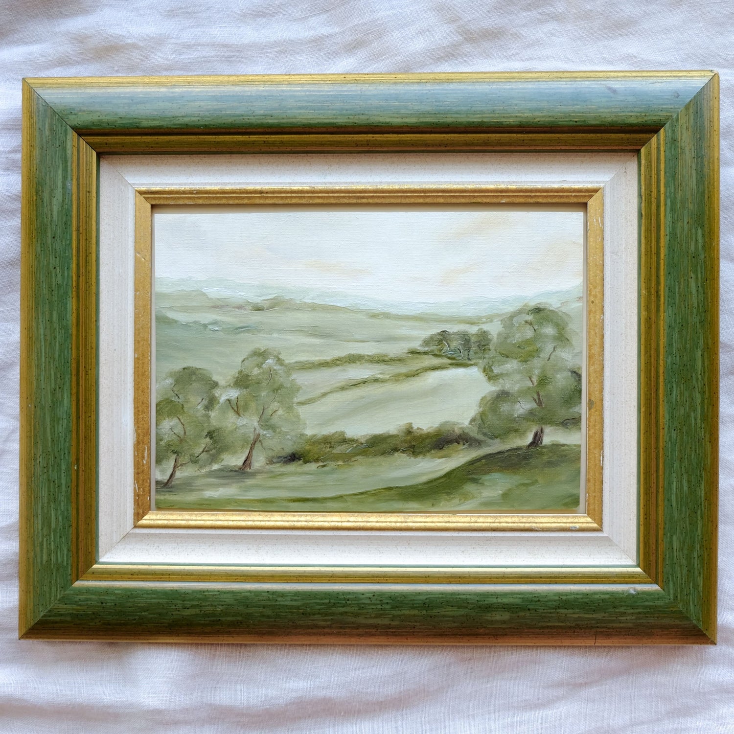 five landscape paintings arranged in a grid. two have frames (one green, one gold and ornate). the others are gallery canvases. all depict various English countryside landscapes with soft greens and blues. 